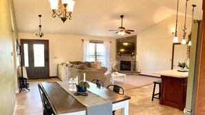 A spacious living room with a fireplace, a dining area with a long table, and a kitchen area.