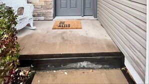 A grey front door with a stone wall and a wicker bench to the left.