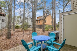 A backyard with a blue table and four chairs, surrounded by trees and a house.