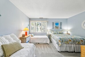 A bedroom with two beds, a window with blinds, a lamp, and a wall-mounted picture.