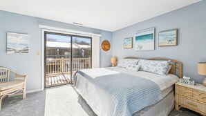 A bedroom with a bed, a nightstand, a chair, a balcony, and artwork on the walls. - Cozy Sea Pines Getaway! Features Community Pool and Short Walk to The Beach. (Bethany Beach)
