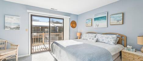 A bedroom with a bed, a nightstand, a chair, a balcony, and artwork on the walls.