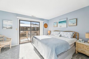 A bedroom with a bed, a nightstand, a chair, a balcony, and artwork on the walls.