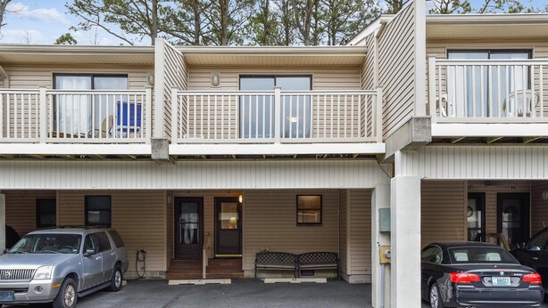 A two-story building with a covered parking area, a bench, and a small outdoor seating area. - Cozy Sea Pines Getaway! Features Community Pool and Short Walk to The Beach. (Bethany Beach)