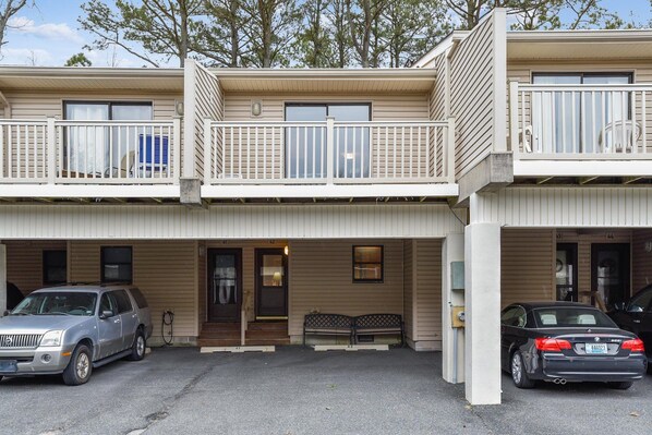 A two-story building with a covered parking area, a bench, and a small outdoor seating area.
