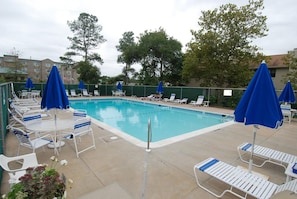 A swimming pool with lounge chairs and umbrellas, surrounded by trees and buildings.