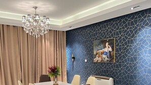 A dining area with a white table, beige chairs, a chandelier, and a patterned wall. - MacDonald Apartments A5  (Lagos)