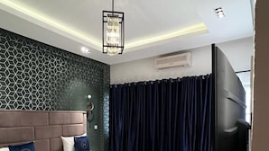A modern hotel room with a large bed, a geometric-patterned wall, a colorful striped rug, and a flat-screen TV. - MacDonald Apartments A5  (Lagos)