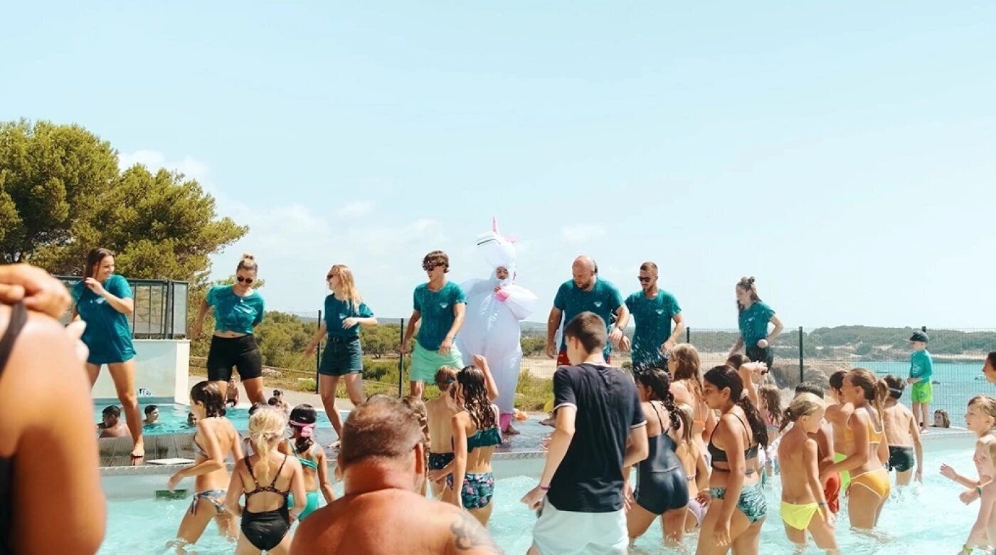A group of people at a swimming pool with a clear view of the sea and trees in the background.