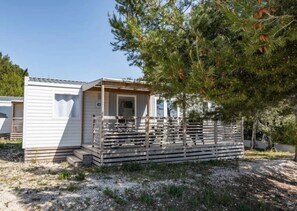 Ein kleines, eingeschossiges Mobilheim mit Veranda und umzäunter Fläche.
