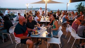 A crowded outdoor dining area with tables and chairs, overlooking a scenic view.