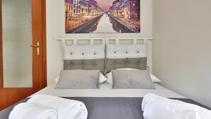 Ein Hotelzimmer mit einem Bett, zwei Kissen, einem Kopfschild mit Punkte-Muster und einem Bild mit Blick auf einen Kanal an der Wand.