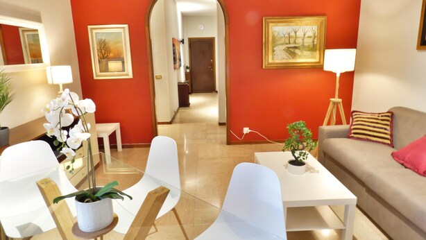 Ein modernes Wohnzimmer mit roter Akzentwand, weißen Möbeln und Blick in den Flur.