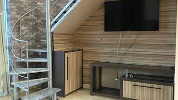 A modern living room with a spiral staircase, a flat-screen TV mounted on the wall, and a wooden entertainment unit.
