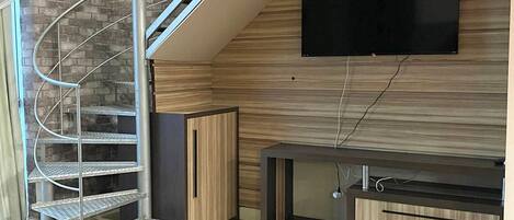 A modern living room with a spiral staircase, a flat-screen TV mounted on the wall, and a wooden entertainment unit.