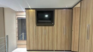 A modern bedroom with a bed, a TV mounted on a wooden wardrobe, and a staircase leading to an upper level. - Saint Sebastian Flat 612 - Até 4 pessoas com hidro no centro (Jaragua do Sul)