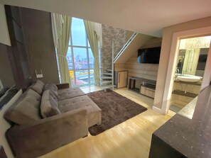 Ein modernes Wohnzimmer mit großem Fenster, einer Couch, einem Kamin und einer Küchenzeile.