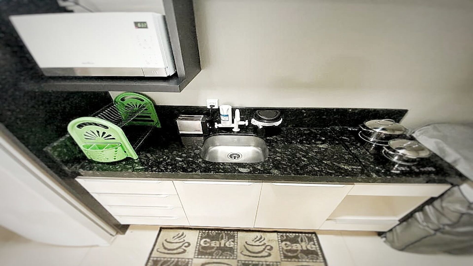 Una cocina con un lavamanos, un escurreplatos verde y una cafetera.
