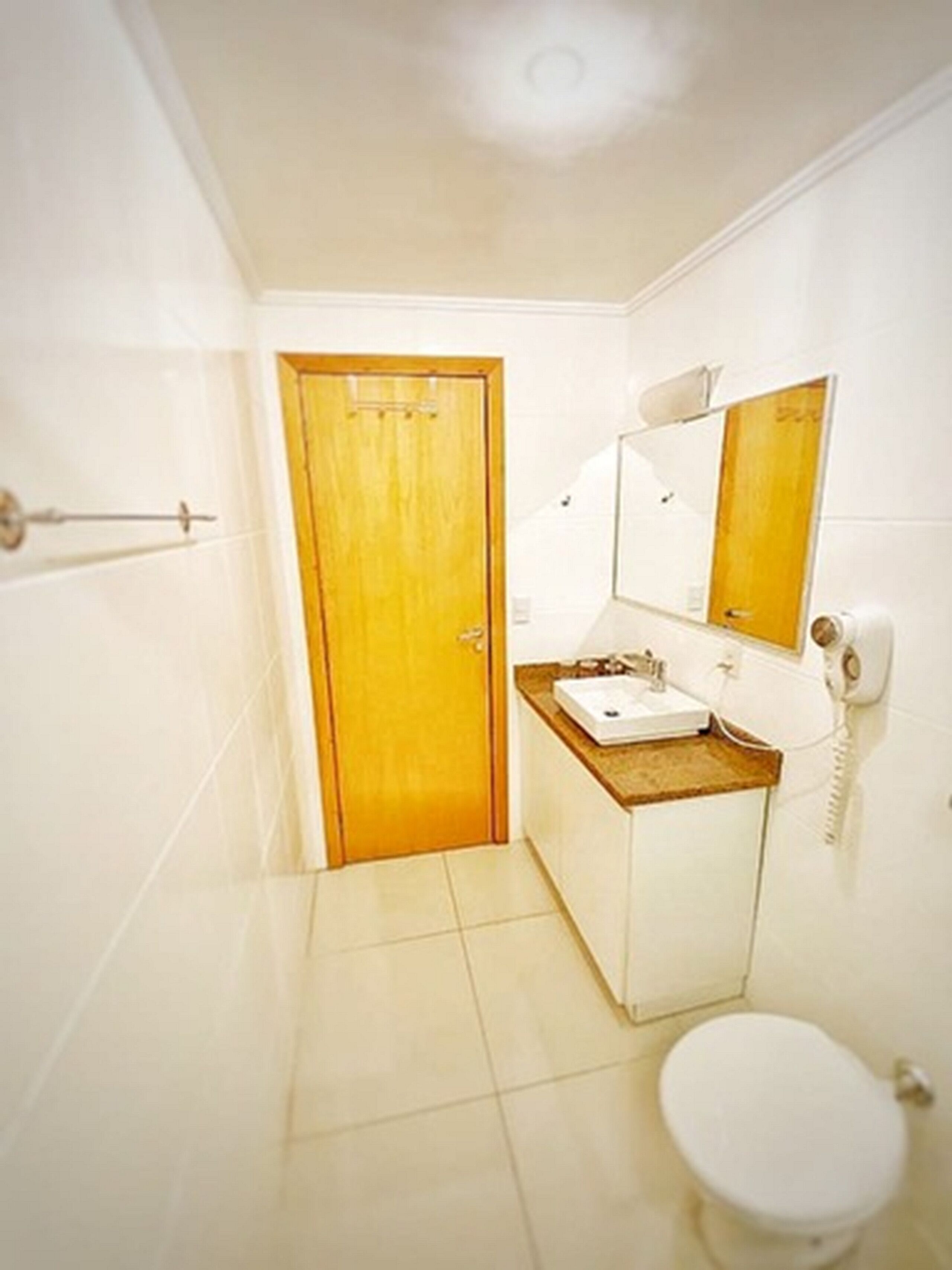 Un baño con puerta de madera, inodoro blanco, lavamanos con espejo y teléfono.