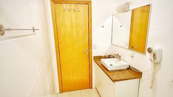Un baño con puerta de madera, inodoro blanco, lavamanos con espejo y teléfono.