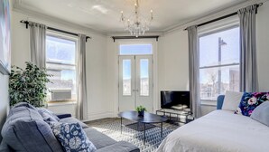 A modern hotel room with a large bed, a sofa, a TV, and a chandelier. - Chez Mont Royal Apartments (Montreal)