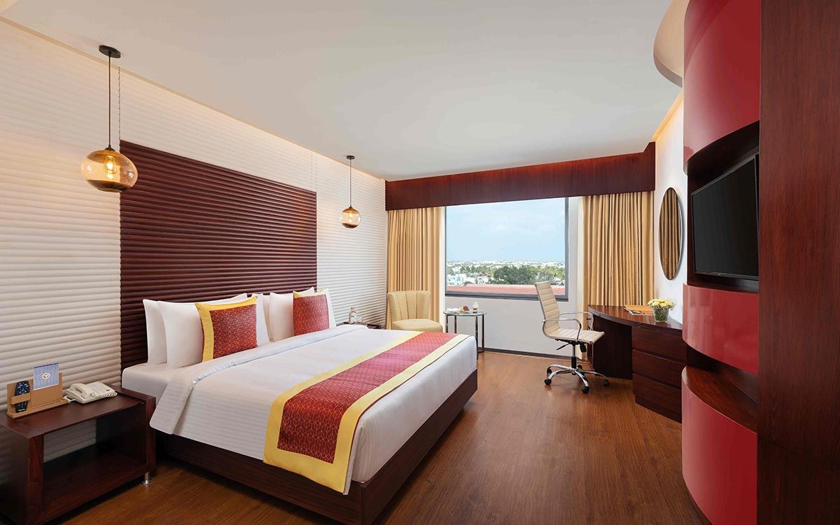 Habitación de hotel con una cama grande, un escritorio con silla, un televisor y vistas a la ciudad.