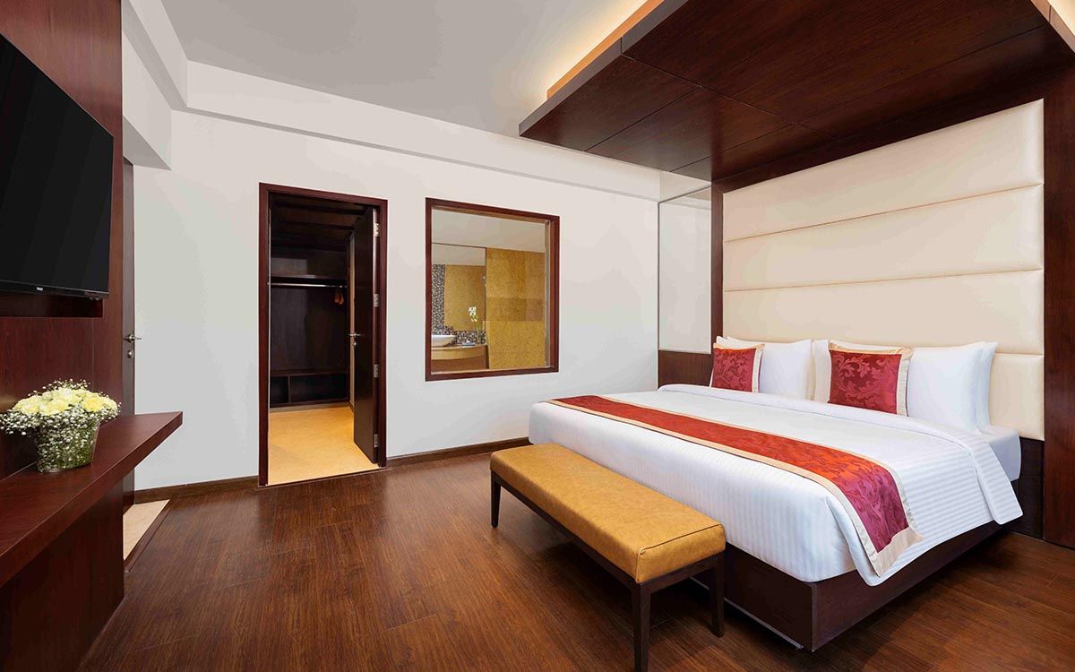 Habitación de hotel con una cama grande, un banco, un televisor, un armario y un espejo.