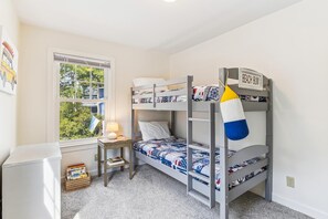 Habitación con literas, un escritorio, una lámpara y una ventana con vistas a árboles.