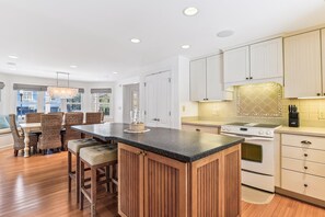 A modern kitchen with a central island, wooden cabinets, and a dining area with wicker chairs.