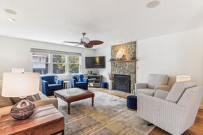 Ein Wohnzimmer mit Kamin, blauen Sesseln, einem gestreiften Sofa und einem an der Wand befestigten Fernseher.
