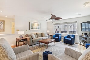 Una sala de estar con sofá, sillones, una mesa de centro, televisor y ventilador de techo.