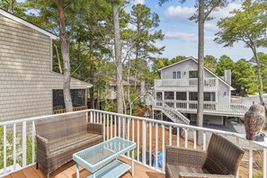 A wooden deck with wicker furniture and a white railing overlooking a residential area with multiple houses and tall trees.