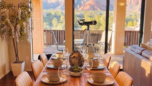 Un comedor con una mesa de madera dispuesta para seis personas, rodeada de sillas de cuero, y un telescopio en un balcón.