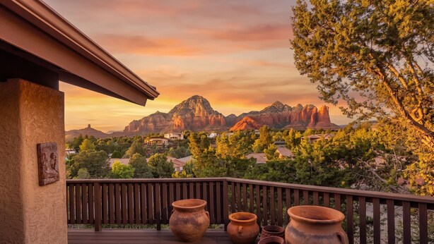 Terraza de madera con macetas de barro, con vistas a un paisaje montañoso con casas y árboles.