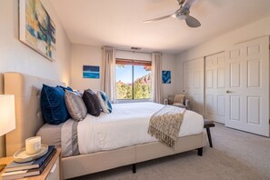 Un dormitorio con una cama, ventilador de techo, ventana con cortinas y una puerta.