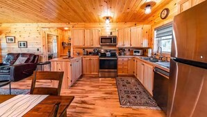 A cabin-style kitchen with wooden cabinets, a stainless steel refrigerator, and a dining area with a table and chairs. - Charming All Wood InteriorAdirondak Cottage (Malone)