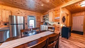 A wooden cabin interior with a dining table, chairs, a refrigerator, and a kitchen area. - Charming All Wood InteriorAdirondak Cottage (Malone)