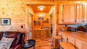 A wooden cabin interior with a kitchen area, a dining table, and a leather couch. - Charming All Wood InteriorAdirondak Cottage (Malone)