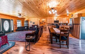 Un intérieur spacieux de chalet en bois, comprenant un coin repas, une cuisine et un salon.