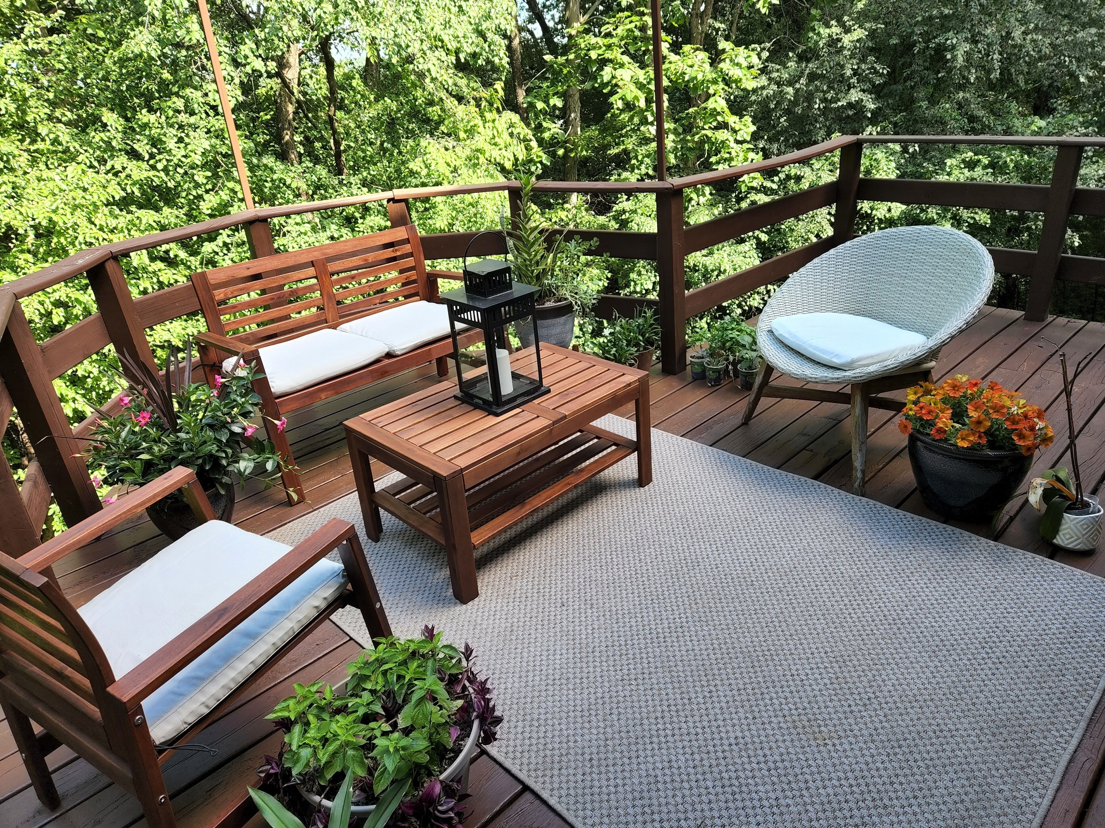 Une terrasse en bois avec un banc, une chaise en osier et une table sur laquelle est posée une lanterne.
