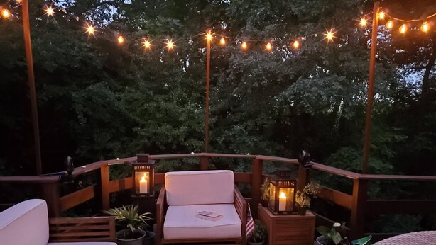 A deck with a sofa, a chair, and a small table, surrounded by potted plants and string lights. - Large Home close to everything, Dogs welcome. (Fitchburg)