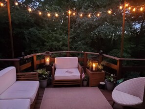 A deck with a sofa, a chair, and a small table, surrounded by potted plants and string lights. - Large Home close to everything, Dogs welcome. (Fitchburg)