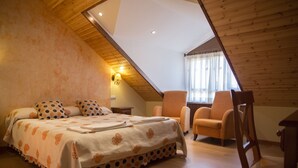 Quarto com teto inclinado, cama com roupa de cama de bolinhas, uma cadeira e uma mesa de cabeceira.