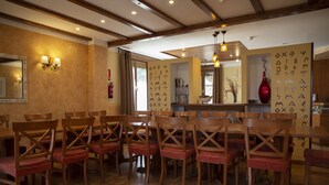 Uma sala de jantar com cadeiras de madeira e uma mesa grande, vigas de madeira no teto e luminárias fixadas na parede.