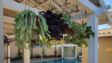 Área externa coberta com piscina, plantas pendentes, extintor de incêndio e mesa com cadeiras.