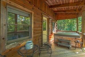 A wooden cabin with a covered porch, a hot tub, and a dining table with chairs.