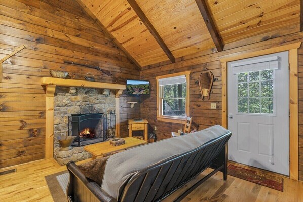 A log cabin interior with a stone fireplace, wooden walls, a bench, and a door.