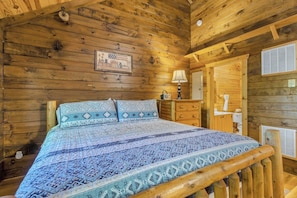 A wooden cabin room with a bed, dresser, and a door leading to another room.