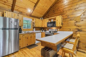 A wooden cabin kitchen with a refrigerator, microwave, stove, and wooden cabinets.