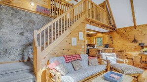 A wooden cabin interior with a stone wall, wooden staircase, sofa, chairs, and a dining table. - Cabin #1 - Fantasy Hideaway (Stanardsville)